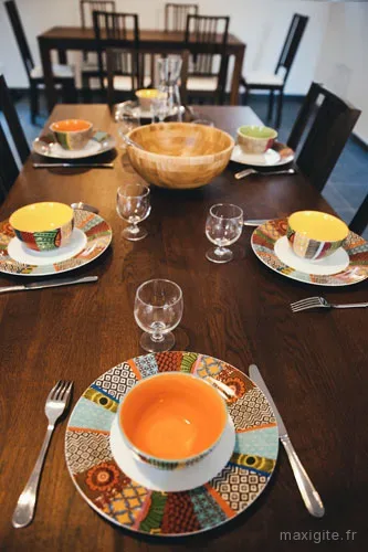 Salle a manger claire avec grande table en bois et vaisselle coloree dressee