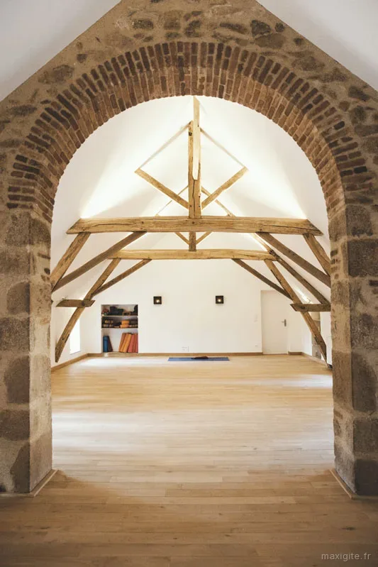 Salle de yoga sous charpente en pierre et bois avec tapis au sol