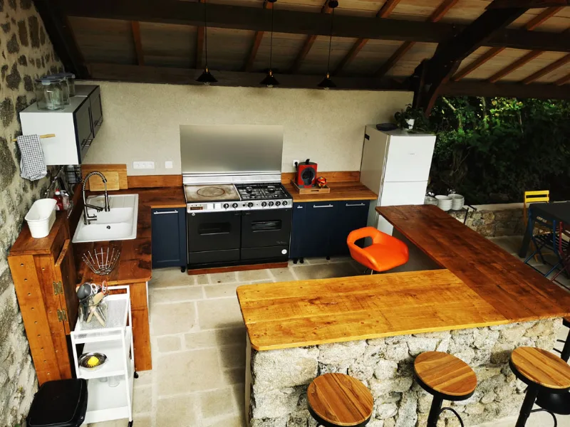 Cuisine d'ete exterieure sous le preau avec piano de cuisson et bar en bois