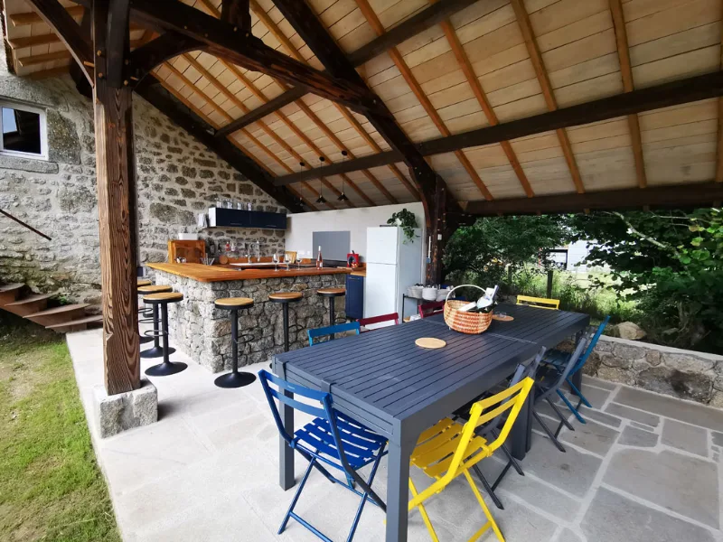 Grande table exterieure sous le preau avec chaises colorees pour les repas en groupe