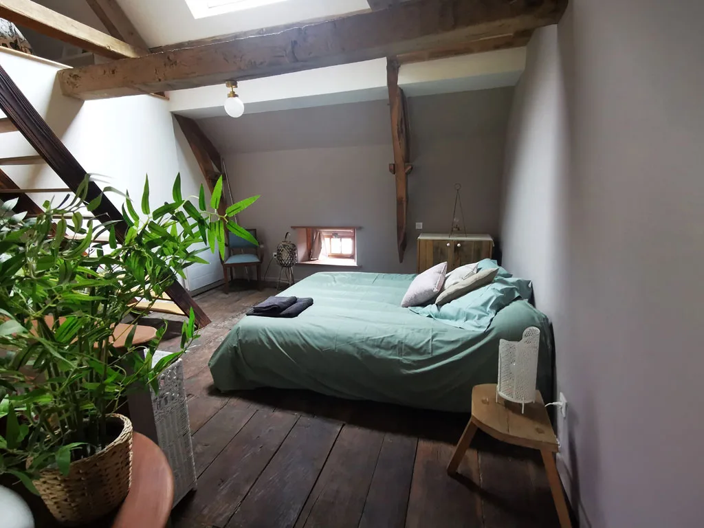 Chambre mansardee sous charpente en bois avec lit double et parquet ancien