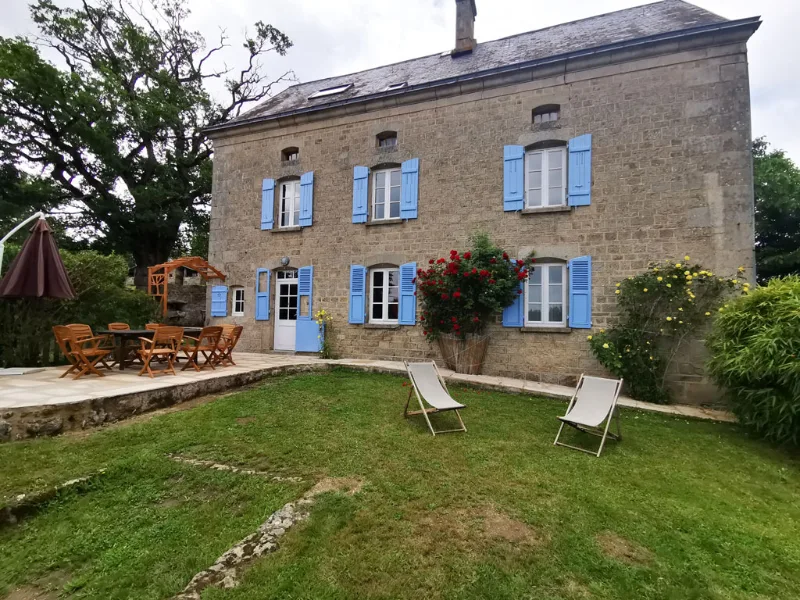 Facade en pierre du domaine avec volets bleus, jardin fleuri et transats