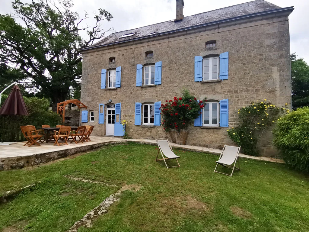 Gîte de groupe Domaine du 20 Malleteix à Champagnat — Facade en pierre du domaine avec volets bleus, jardin fleuri et transats, capacité 22 personnes