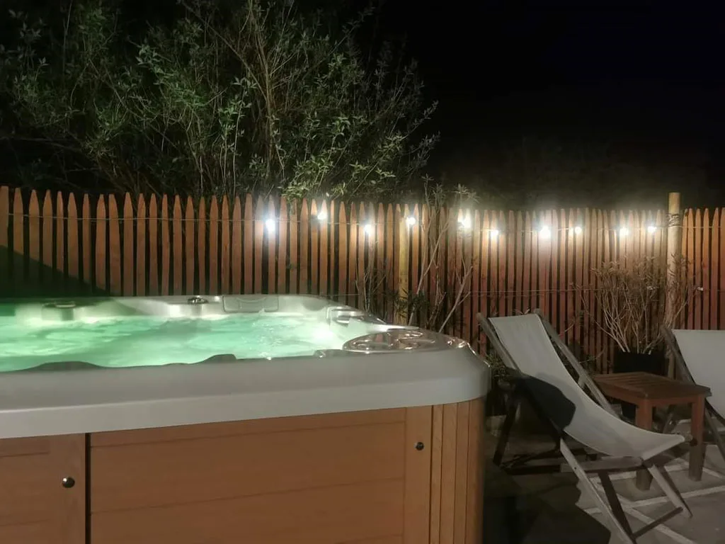 Jacuzzi exterieur eclaire en soiree, entoure d'une cloture en bois