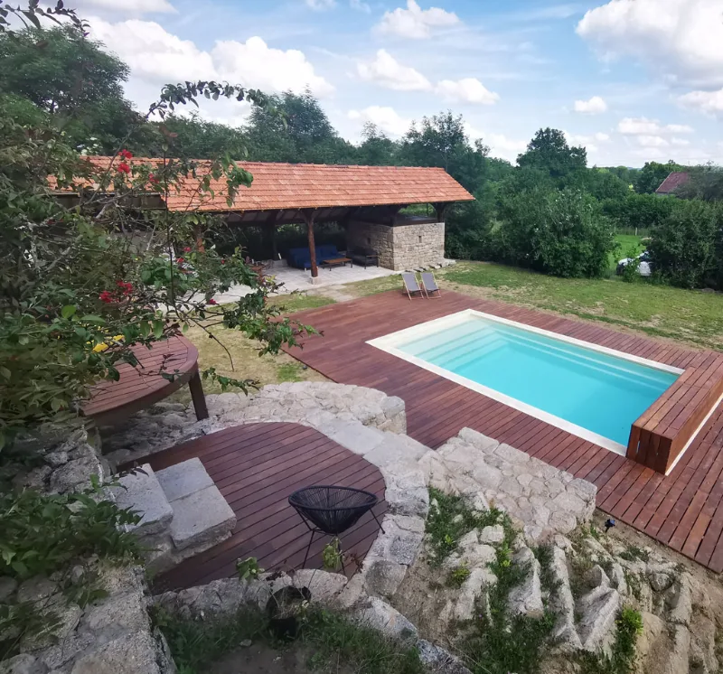 Vue d'ensemble sur la piscine chauffee, la terrasse en bois et le preau en pierre