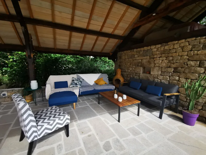 Salon exterieur couvert avec canapes et mur en pierre seche