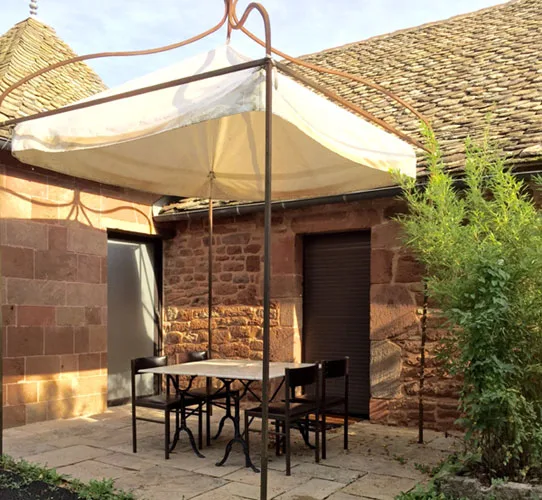 Terrasse extérieure ombragée avec grande table et parasol contre le mur en pierre