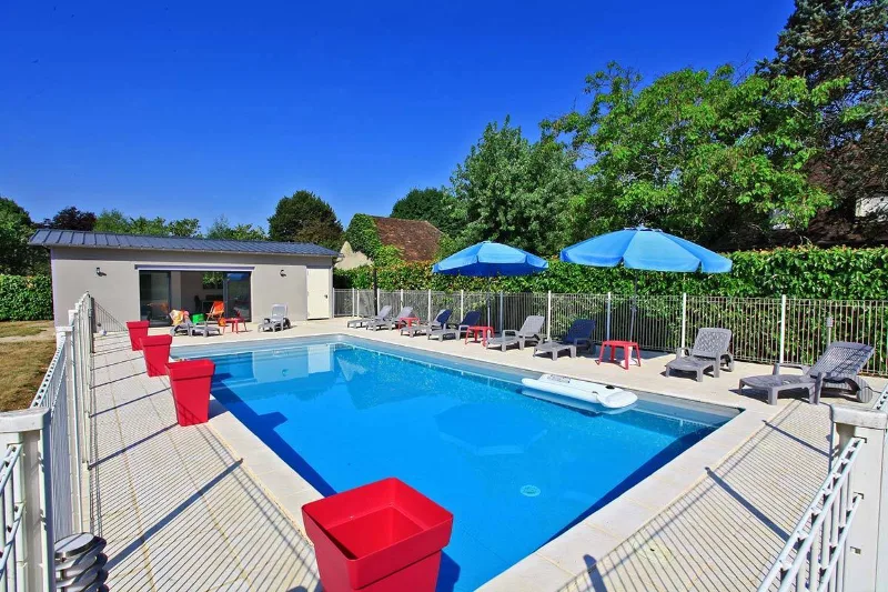 Piscine extérieure et pool house du château vus de loin sous ciel bleu