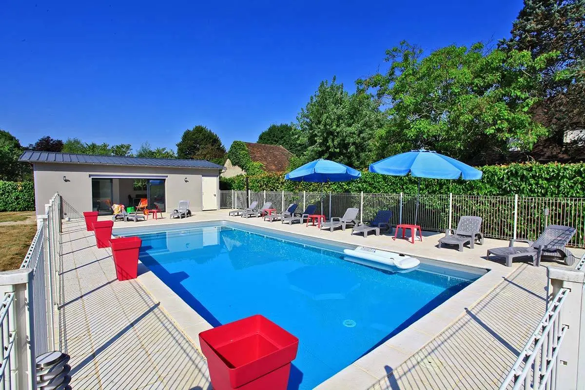 Gîte de groupe Le Château d'Ô à Biars-sur-Cère — Piscine extérieure et pool house du château vus de loin sous ciel bleu, capacité 16 personnes