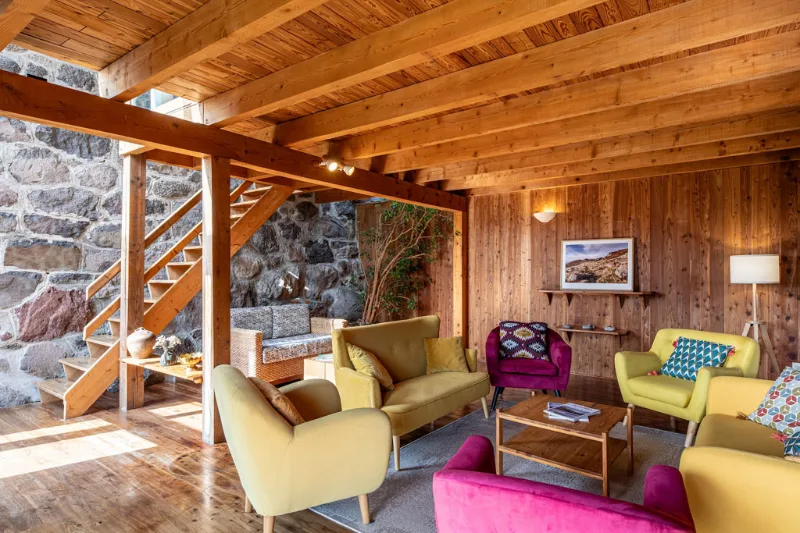 Salon cosy aux murs en bois avec fauteuils jaunes et baie vitrée sur la vallée