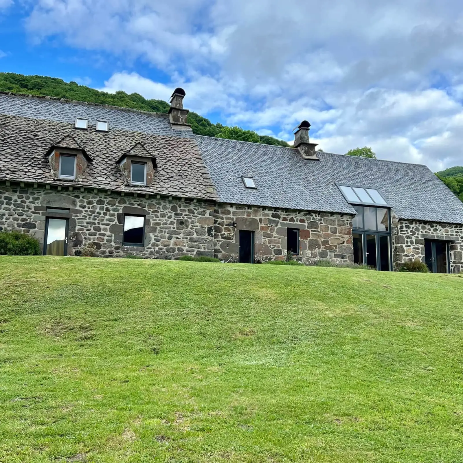 Façade arrière de la maison en pierre vue depuis la pelouse et les arbres