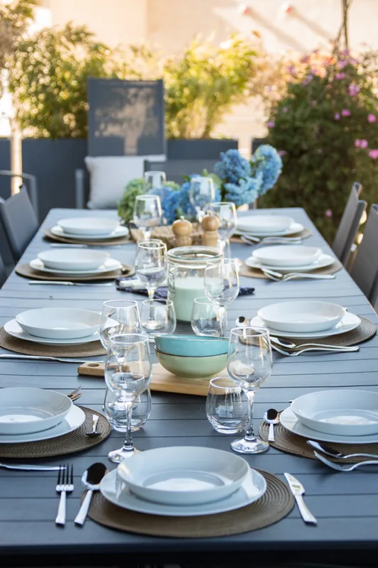Table dressée en extérieur pour un repas de groupe avec fleurs bleues et vaisselle blanche