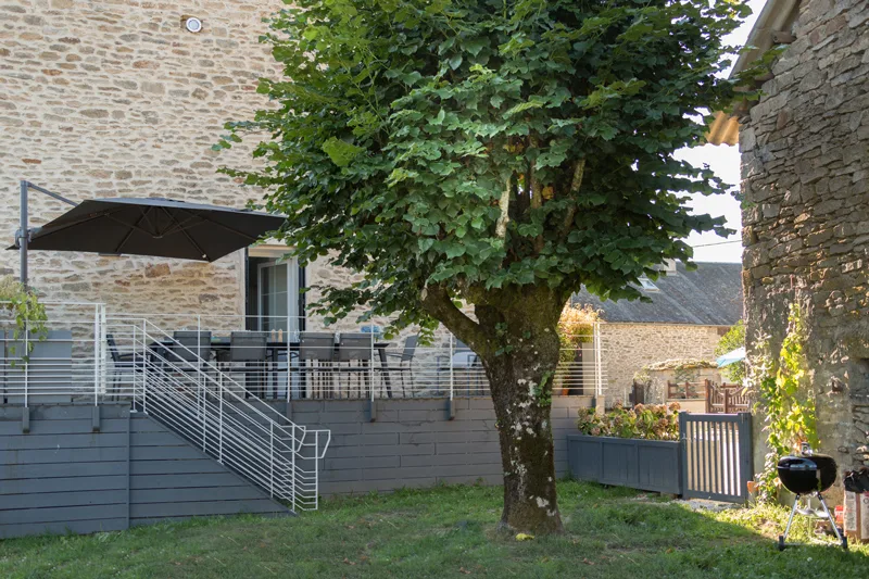 Terrasse extérieure avec parasol, salon de jardin et arbre ombrageant la cour