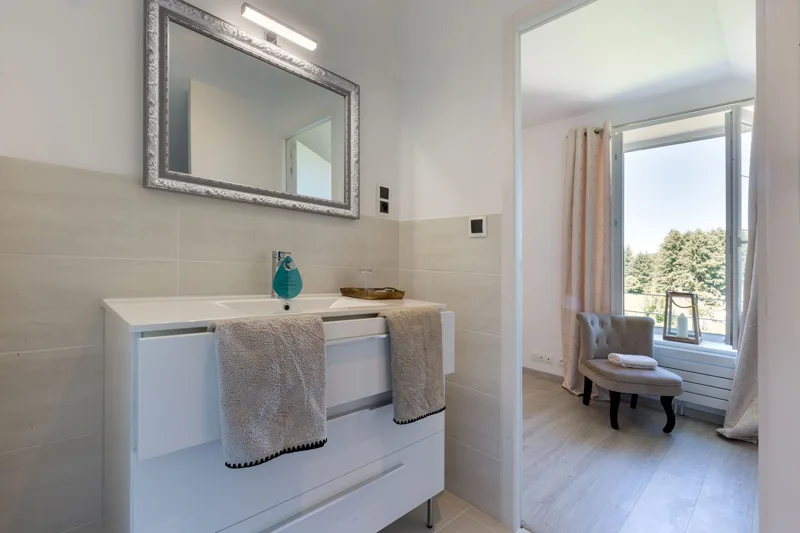 Salle de bain avec double vasque blanche, miroir et vue sur chambre attenante