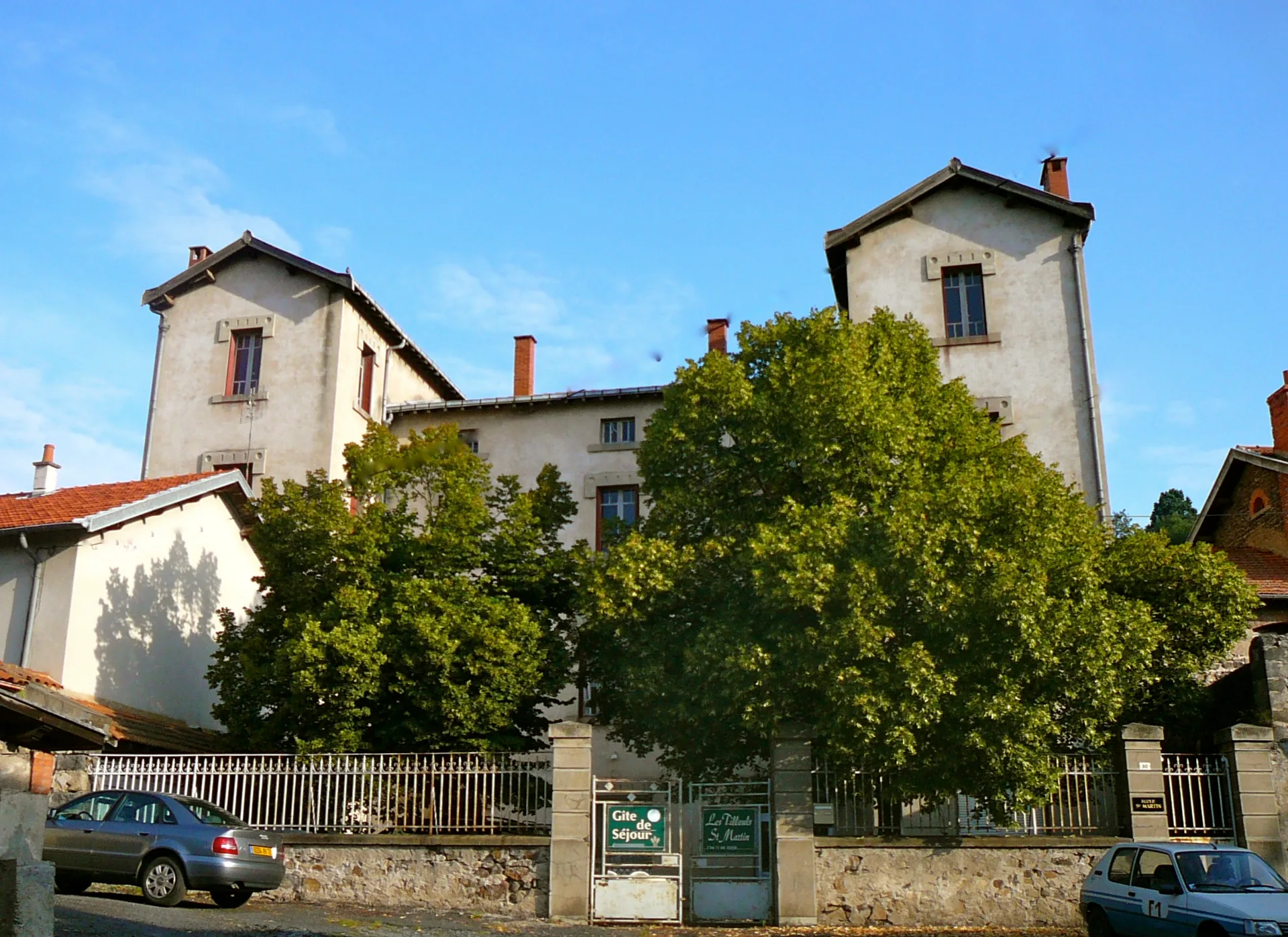 Gîte de groupe Les Tilleuls Saint-Martin à Allègre — Façade de l'ancienne école abritant le gîte, entourée d'arbres, avec son enseigne Gîte de Séjour, capacité 47 personnes