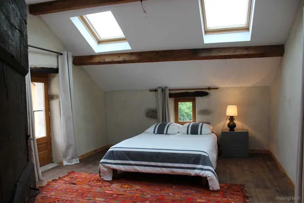 Chambre mansardée avec lit double, poutres apparentes et tapis kilim coloré