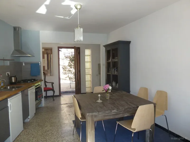 Cuisine ouverte sur salle à manger avec vaisselier bleu et porte donnant sur la terrasse