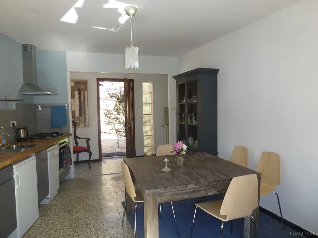 Cuisine ouverte sur salle à manger avec vaisselier bleu et porte donnant sur la terrasse