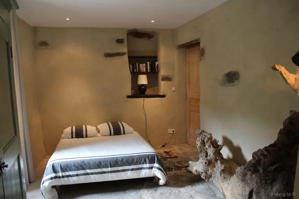 Chambre voûtée en pierre avec niche bibliothèque, lampe et racine de bois sculptée