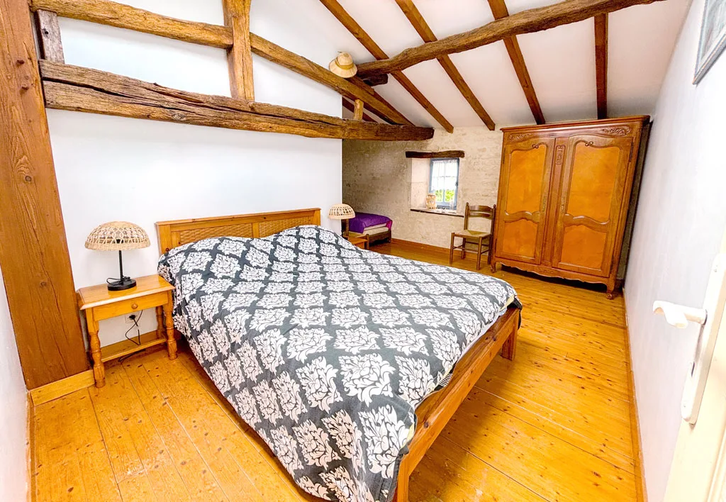 Chambre mansardée avec deux lits simples aux couvre-lits bleus et poutres apparentes