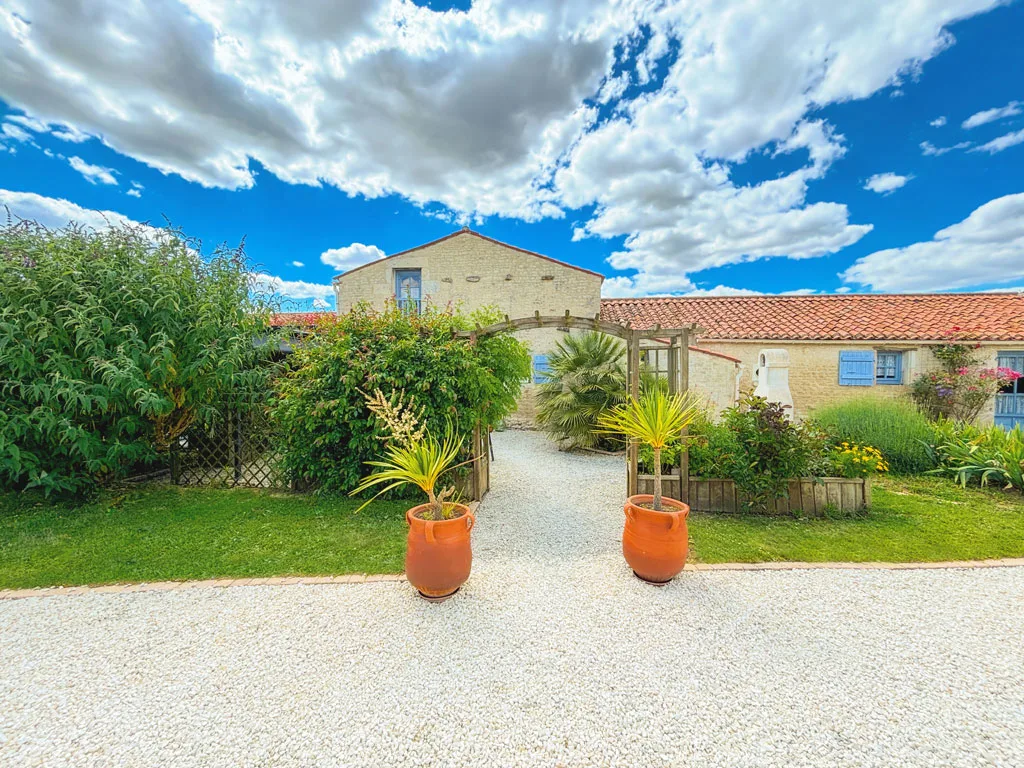 Gîte de groupe Relais de la Haute Mare à Saint-Aubin-la-Plaine — Grande piscine turquoise avec transats et parasols rouges devant la longère en pierre, capacité 23 personnes