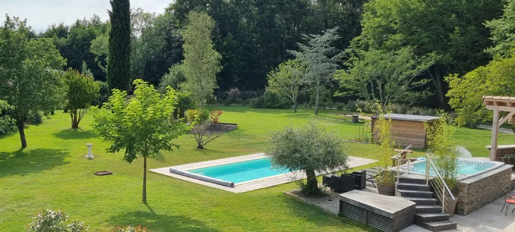 Jardin arboré avec piscine extérieure entourée de pelouse et d'un spa privatif
