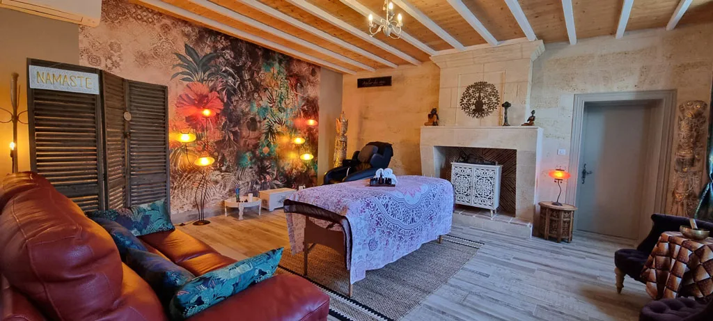 Espace bien-être avec table de massage, fresque murale et fauteuils cocooning