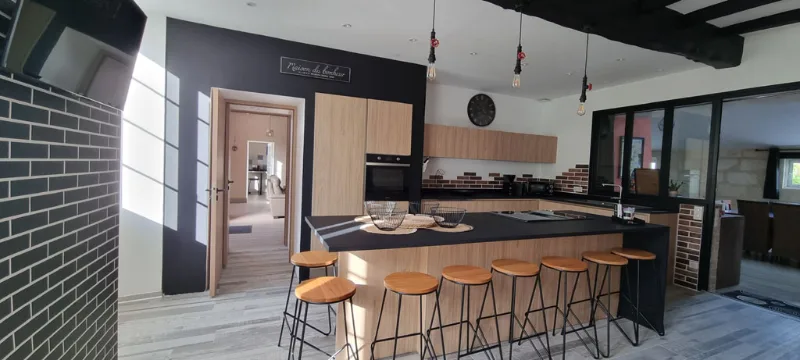 Cuisine ouverte avec îlot central noir et hauts tabourets en bois