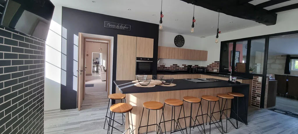 Cuisine ouverte avec îlot central noir et hauts tabourets en bois