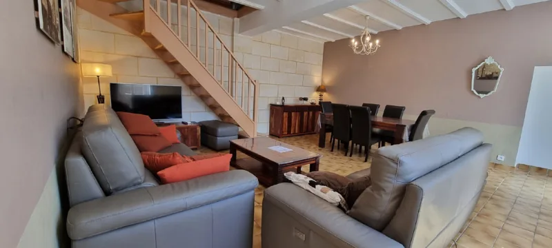Salon avec canapés en cuir, escalier en bois et cheminée en pierre