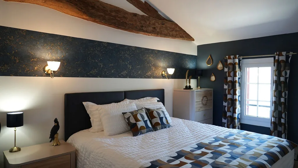 Chambre bleu nuit avec poutre en bois brut et tête de lit capitonnée