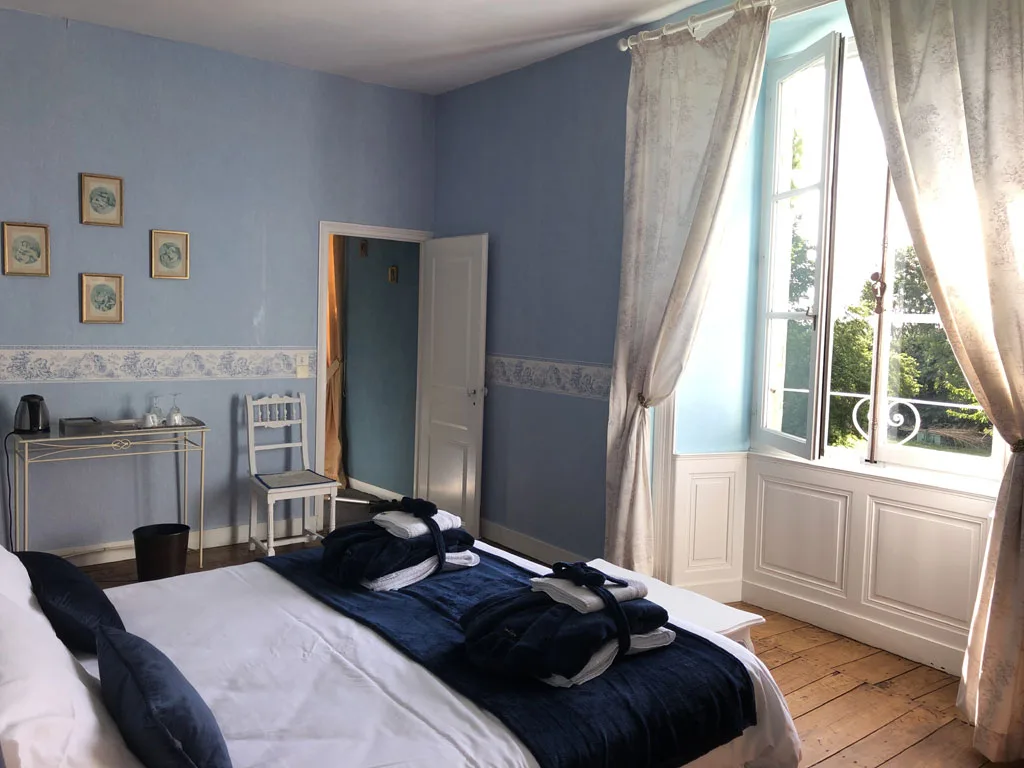 Chambre bleue avec grande fenêtre donnant sur le parc et peignoirs sur le lit