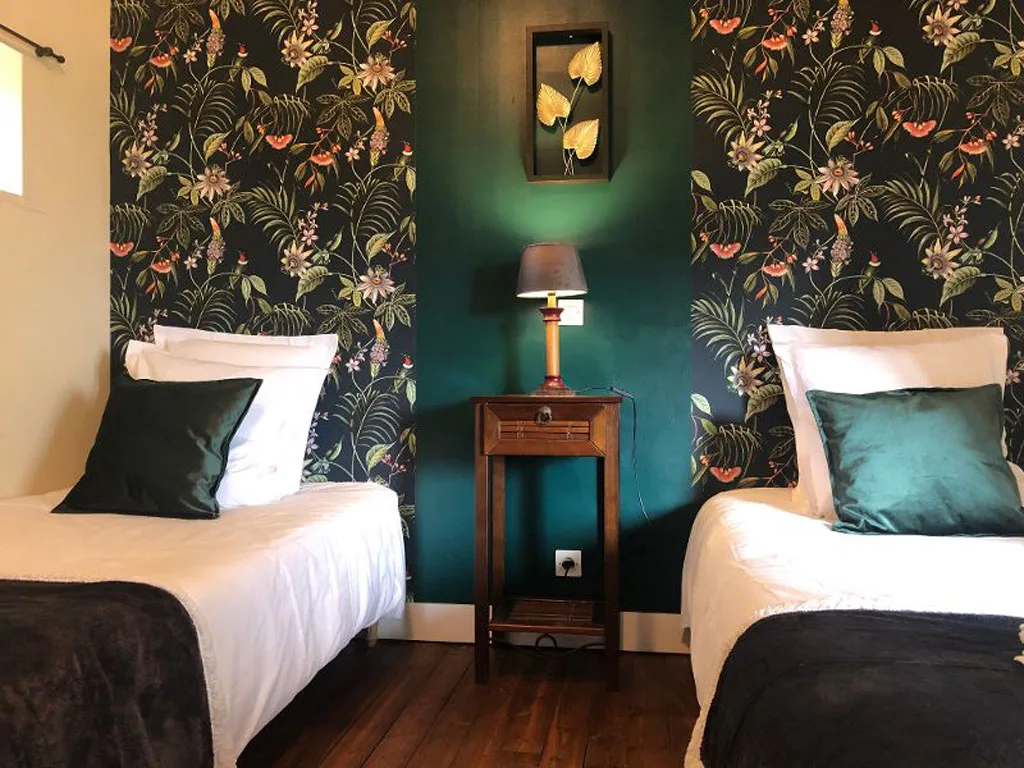 Chambre à lits jumeaux avec papier peint fleuri sombre et coussins verts
