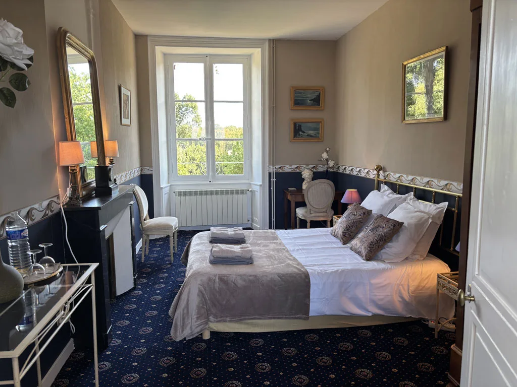 Chambre avec cheminée en marbre, grand miroir doré et vue sur les arbres