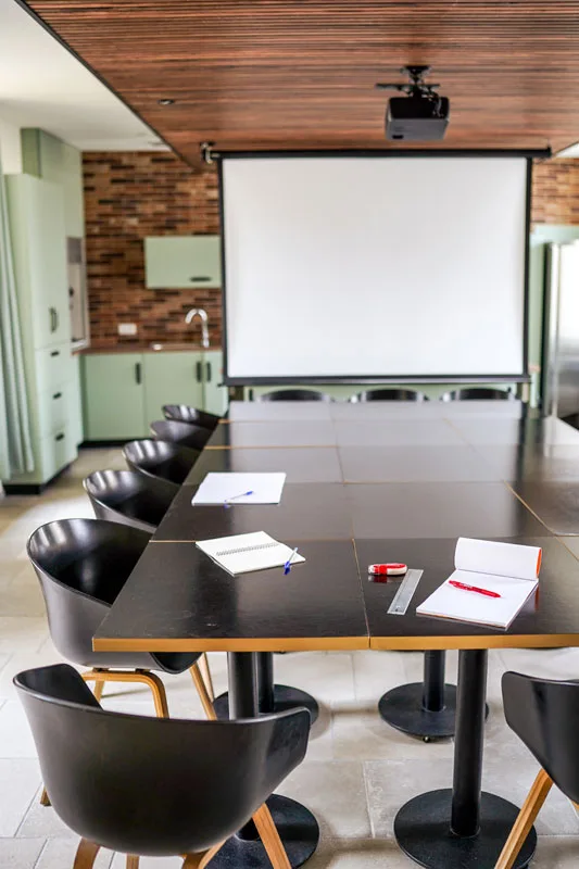Grande salle avec table de réunion, chaises noires et mur en briques apparentes