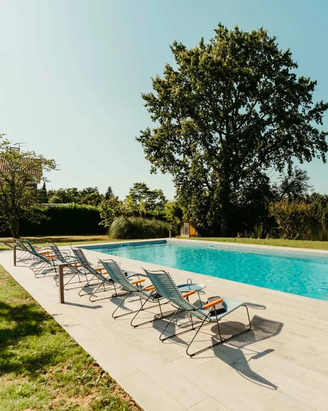 Piscine extérieure entourée de transats face au jardin arboré