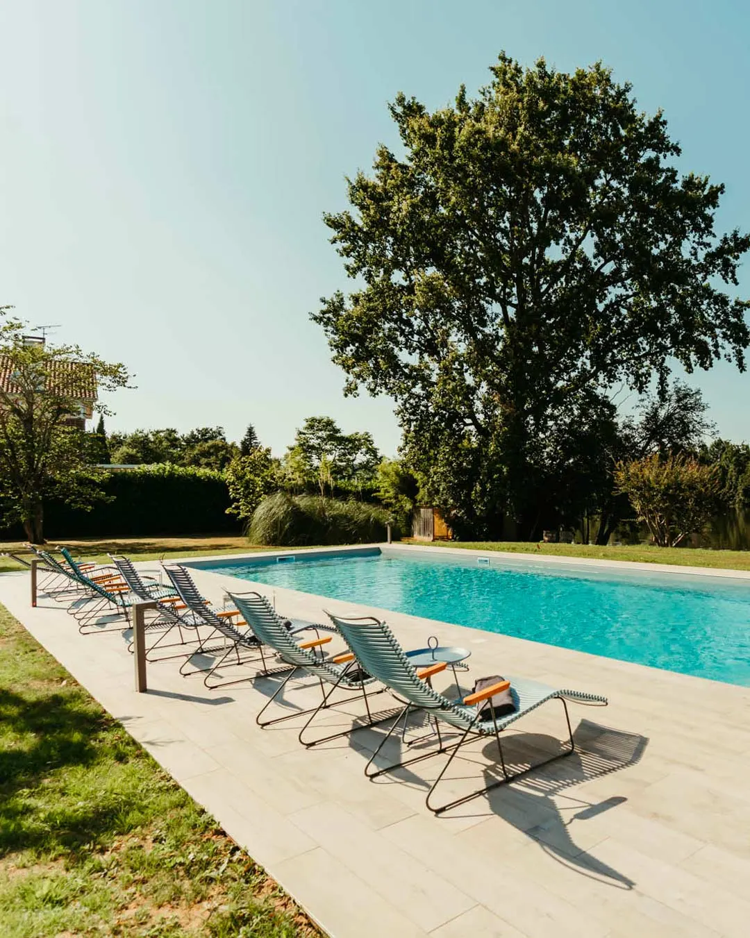 Piscine extérieure entourée de transats face au jardin arboré