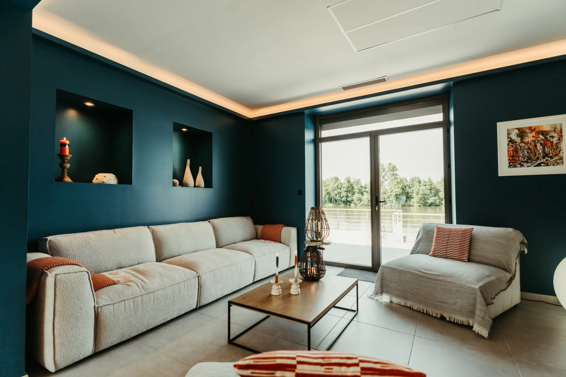 Salon aux murs bleu marine avec canapés et baie vitrée donnant sur la rivière
