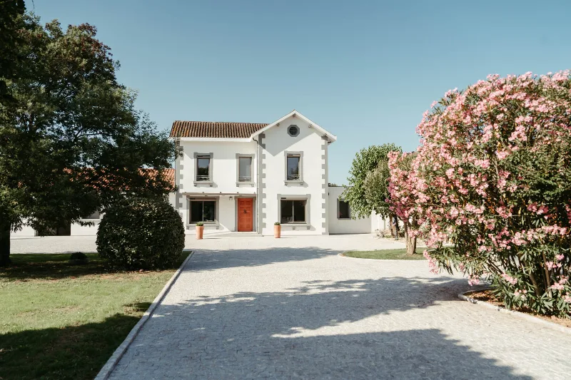 Façade blanche de la Maison de Maître avec allée gravillonnée et jardin fleuri