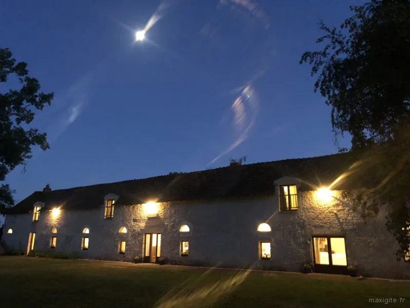 Longue façade en pierre éclairée sous lune avec pelouse et grands arbres au fond