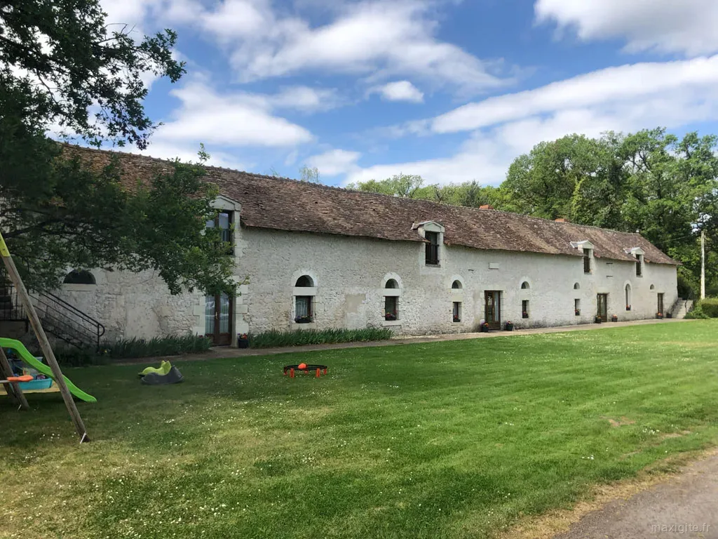 Gîte de groupe Les Vieux Chênes à Oyré — Longue grange rénovée en pierre blanche avec pelouse et balançoires sous ciel bleu, capacité 29 personnes