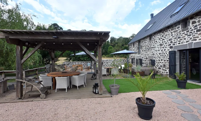 Façade en pierre du gîte avec pergola en bois et terrasse aménagée