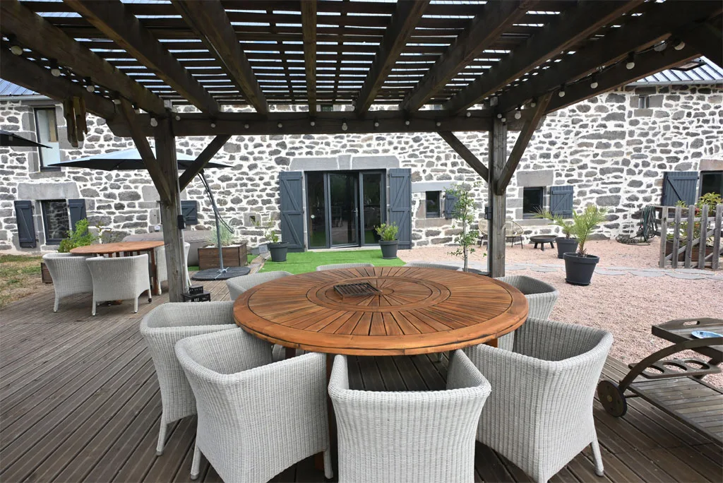 Terrasse couverte sous pergola en bois avec grande table ronde et chaises en osier