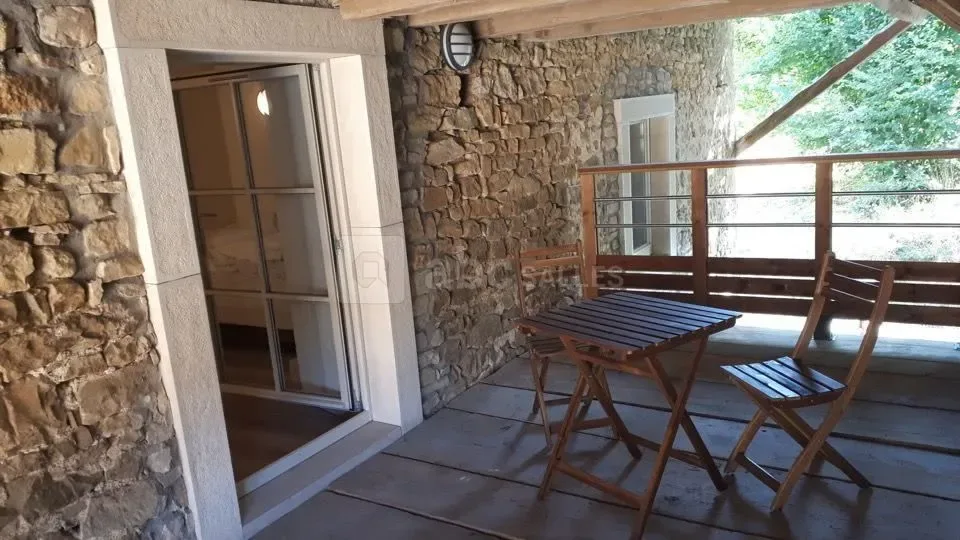 Terrasse en bois à l'étage avec table et chaises pliantes, mur en pierres apparentes