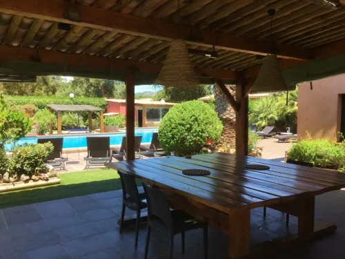 Cuisine d'été couverte avec grande table en bois et vue sur la piscine
