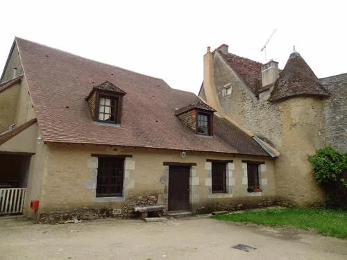 Façade en pierre du gîte avec toiture d'ardoise, lucarnes et volets bleus sous un ciel bleu