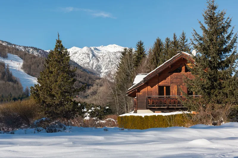 Chalet Le Serre des Oiseaux vu de l'extérieur sous la neige avec les montagnes de Serre Chevalier en arrière-plan
