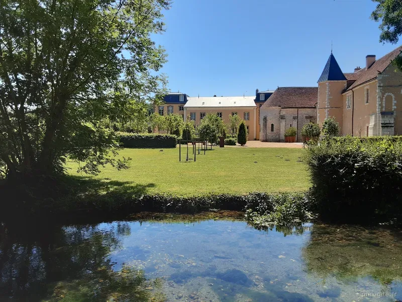 Vue du gîte depuis le parc, pelouse arborée et pièce d'eau au premier plan