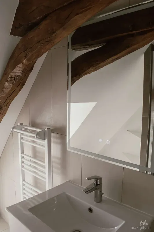 Salle de bain sous combles avec sèche-serviettes et charpente en bois brut
