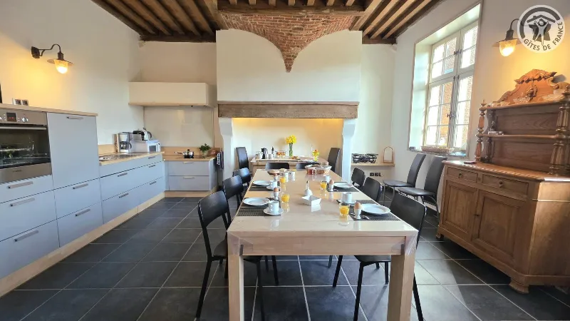 Cuisine ouverte avec grande table dressée pour le petit-déjeuner sous poutres et cheminée voûtée en brique